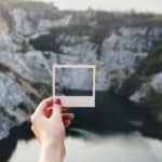 una mano regge la cornice di una polaroid su paesaggio montano